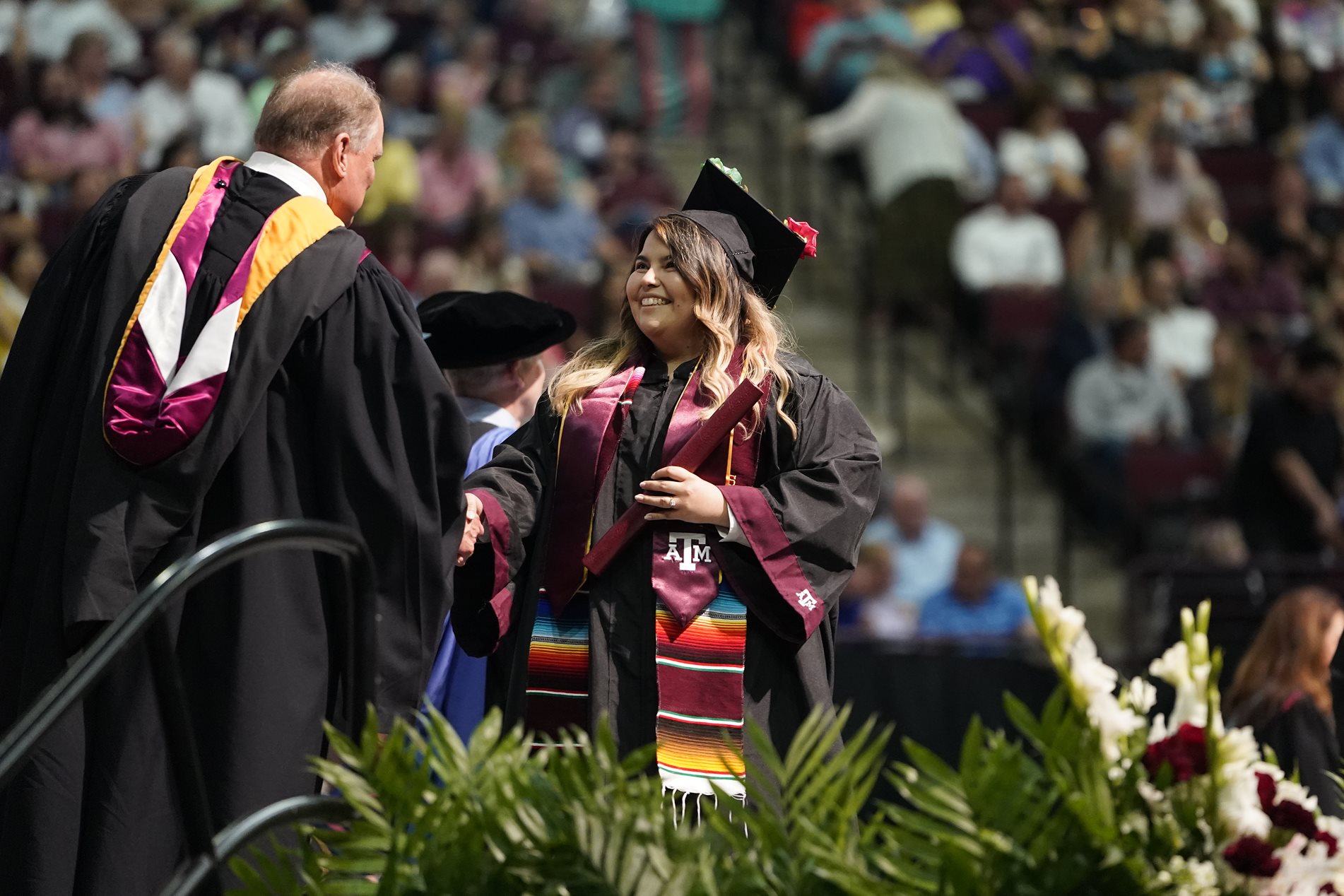 College graduate crossing the stage with smile as she shakes hands with faculty